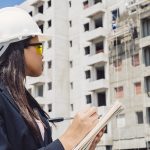 african-american-lady-safety-helmet-writing-notepad-near-building-construction